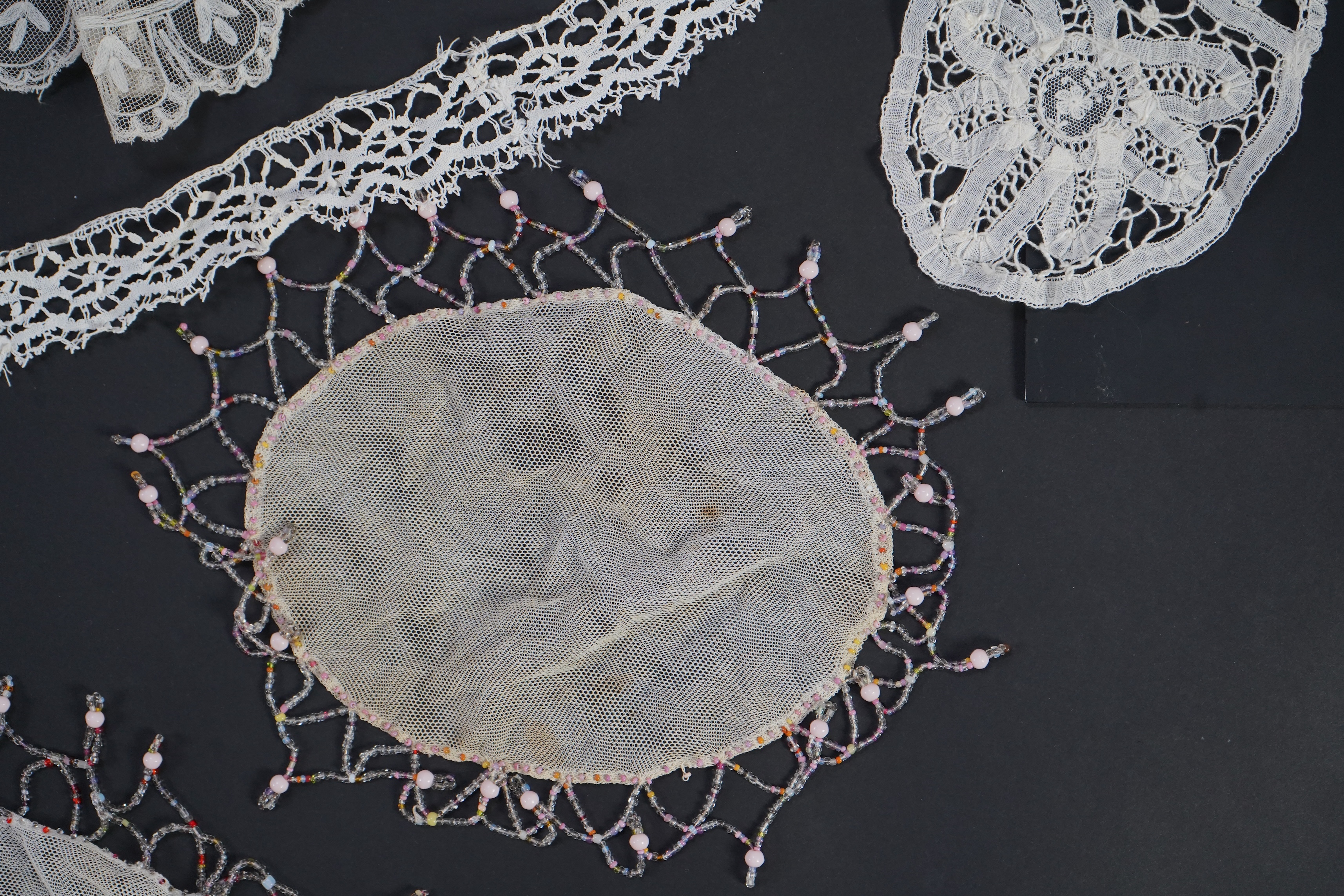 A white tape lace on net bed cover, a cream lace needle run panel, three Brussels bobbin lace collars, a lappet and two beaded tea pot covers, bed cover 200cm x 250cm. Condition - the bedcover has damage to the netting,